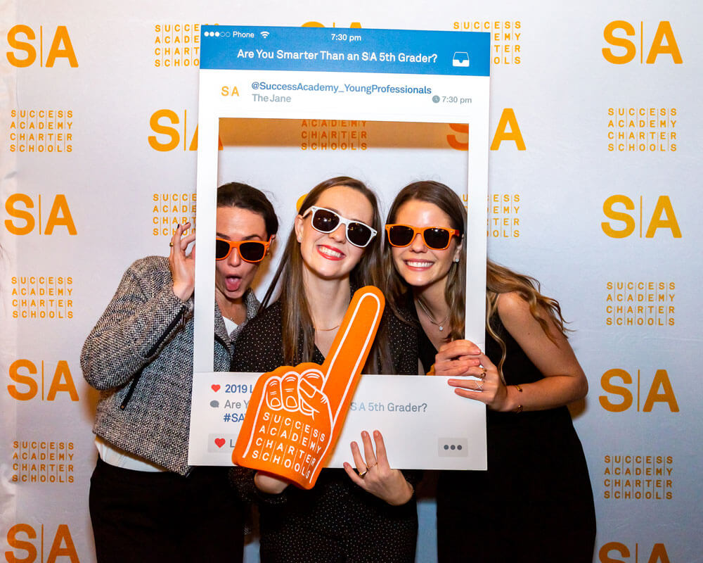 People posing with frame and foam finger, event backdrop.