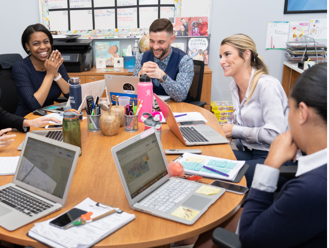 People sitting around table, using laptops, in office meeting.