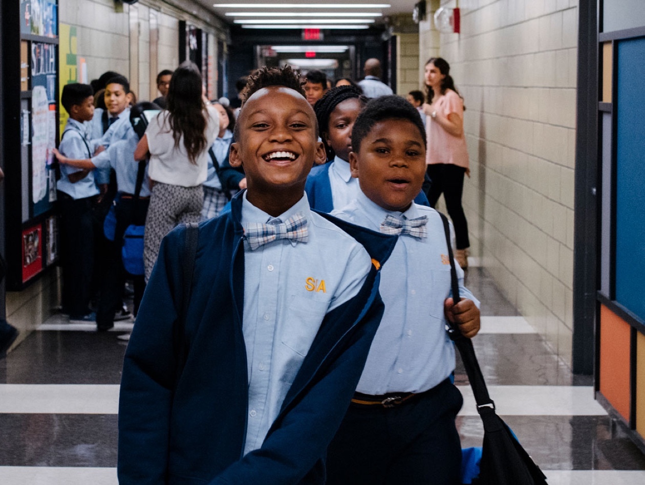 Boys laughing, walking down school hallway with peers around.