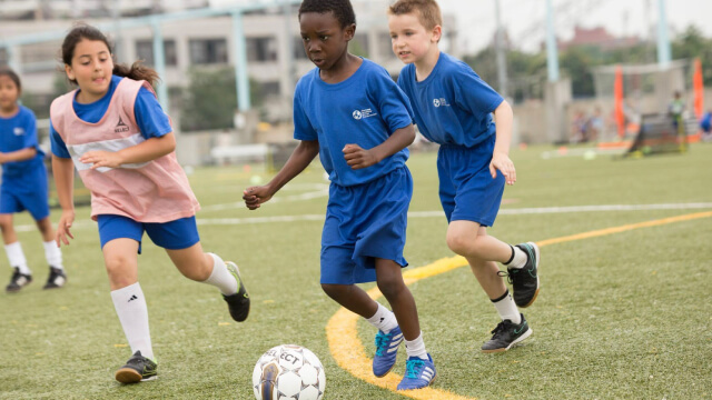 Children playing soccer on a field, wearing blue uniforms.