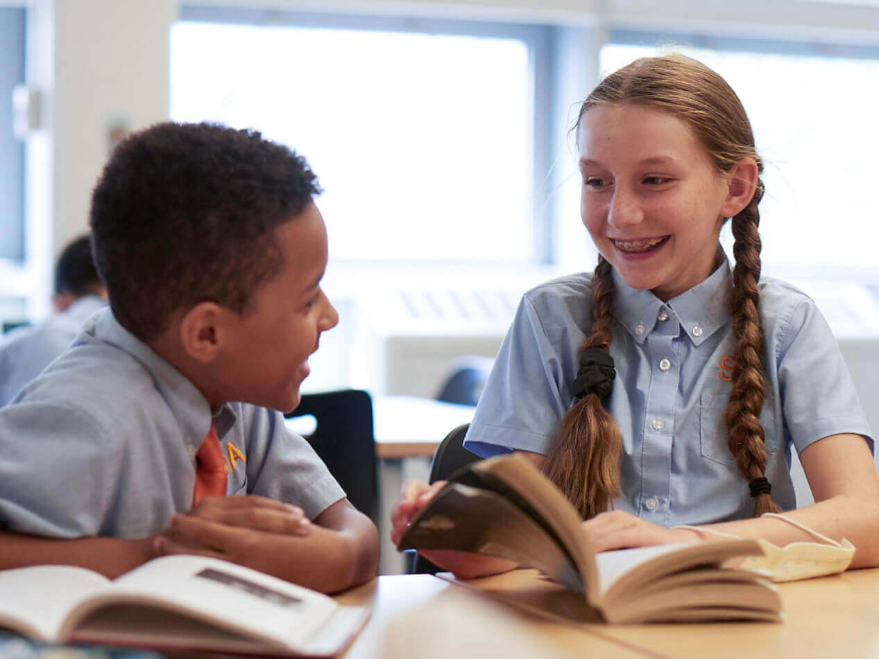 Children read and talk at a classroom table.