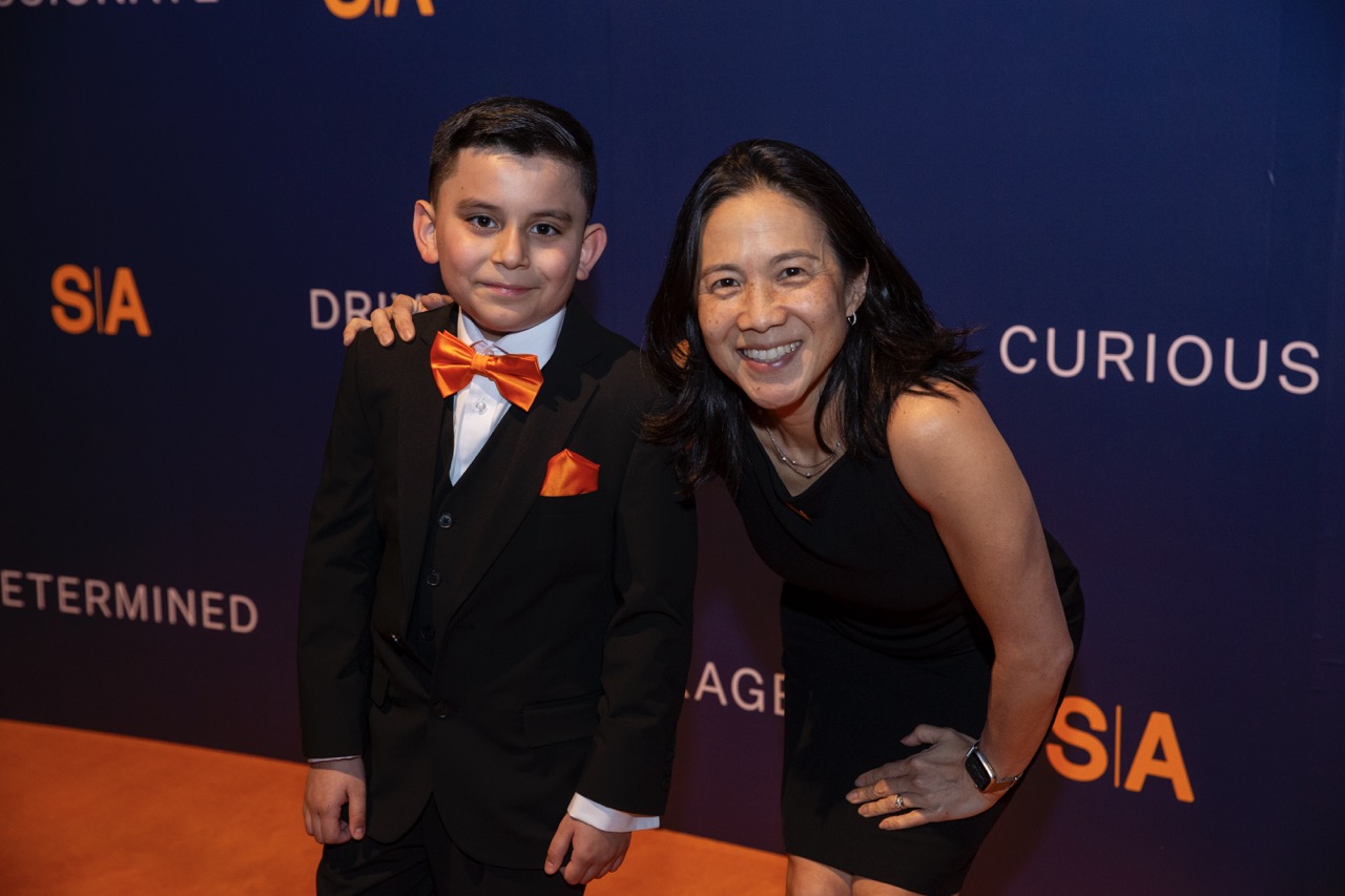 Boy in suit and Dr. Angela Duckworth, New York Times best-selling author, smiling; event backdrop shows 