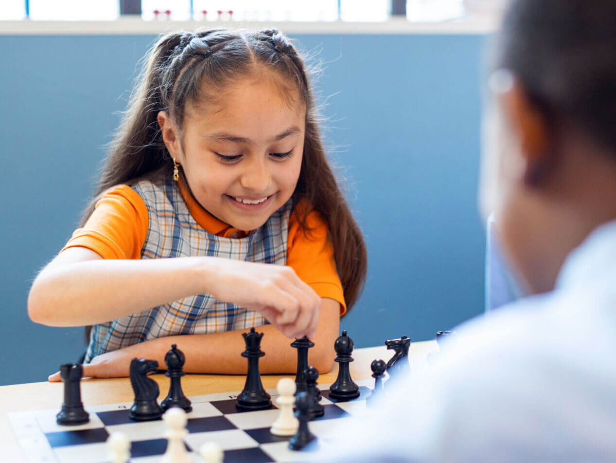 Girl playing chess in classroom, focused and smiling.