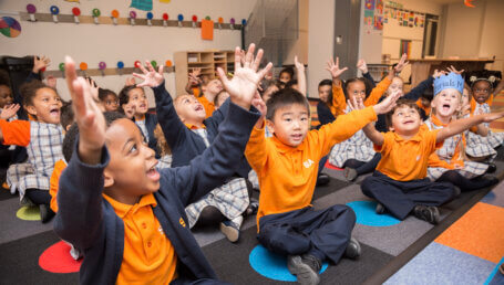 Group of kindergarten students sitting on a colorful rug and participating in a classroom activity.