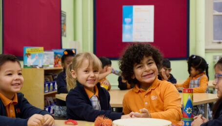 Young children sitting together at a classroom table, smiling and engaged in activities.