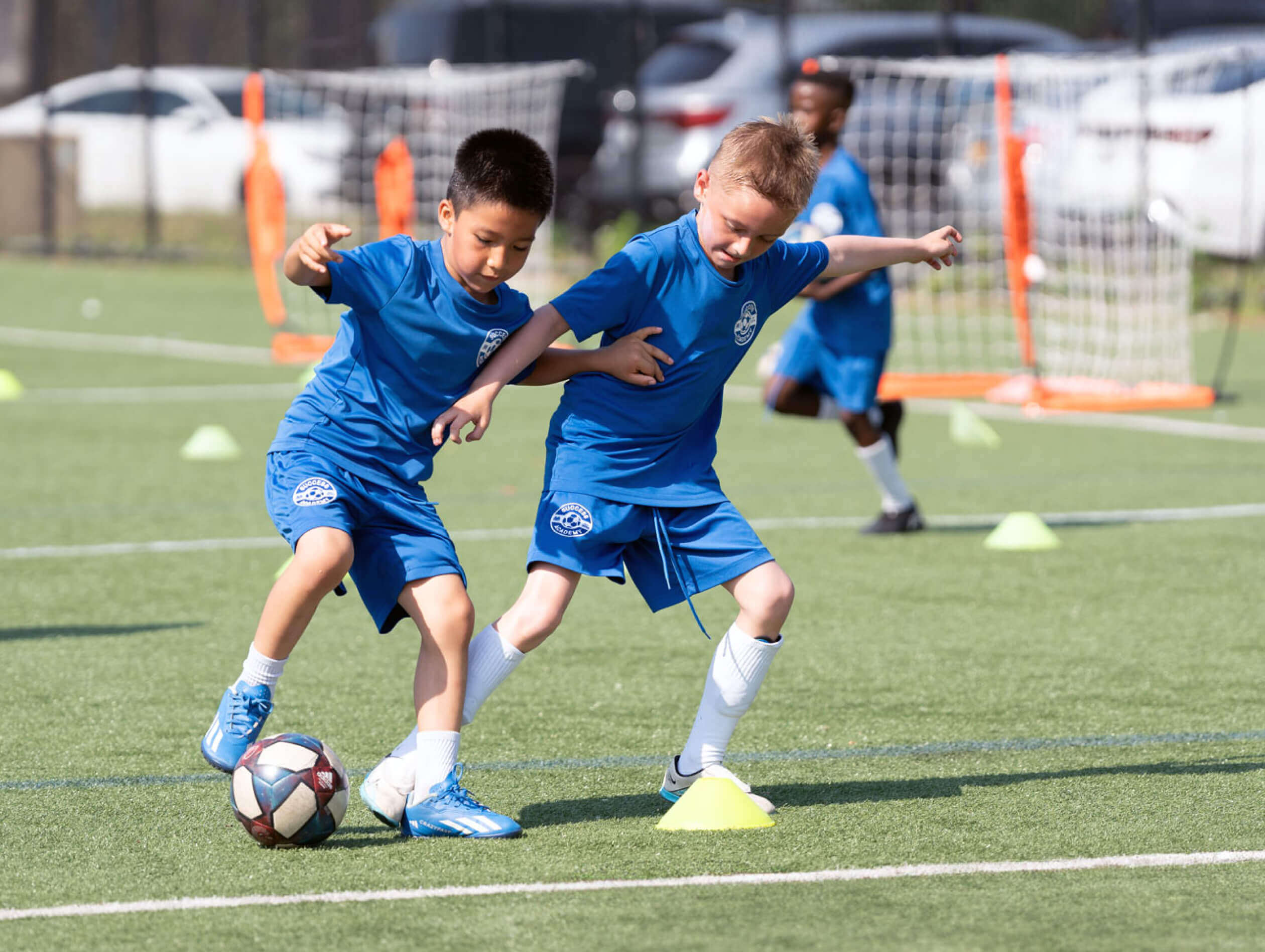 Two young boys in blue uniforms competing for the soccer ball during a game on a grassy field.