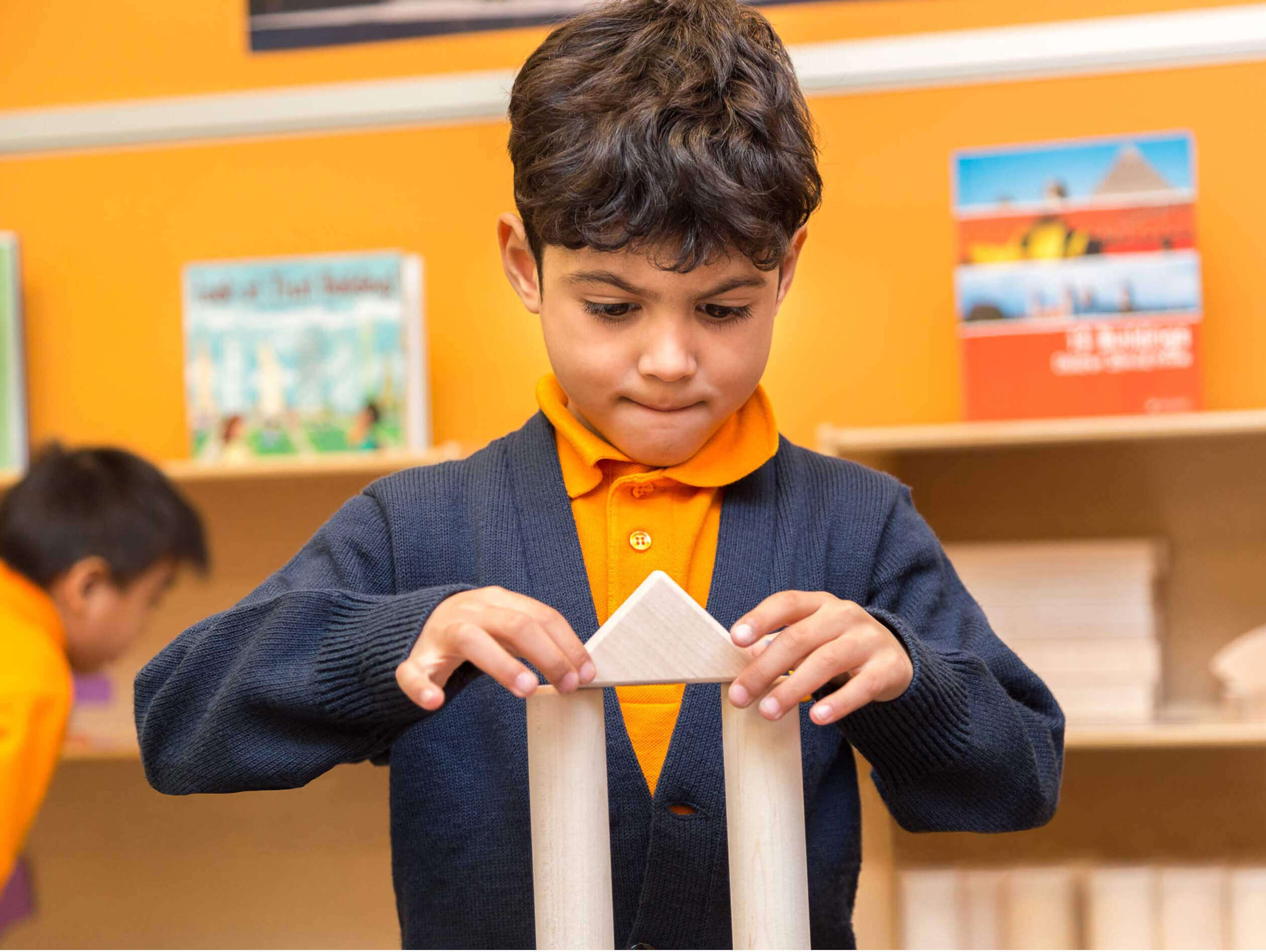 A young boy concentrating on building something with wooden blocks in a classroom setting.
