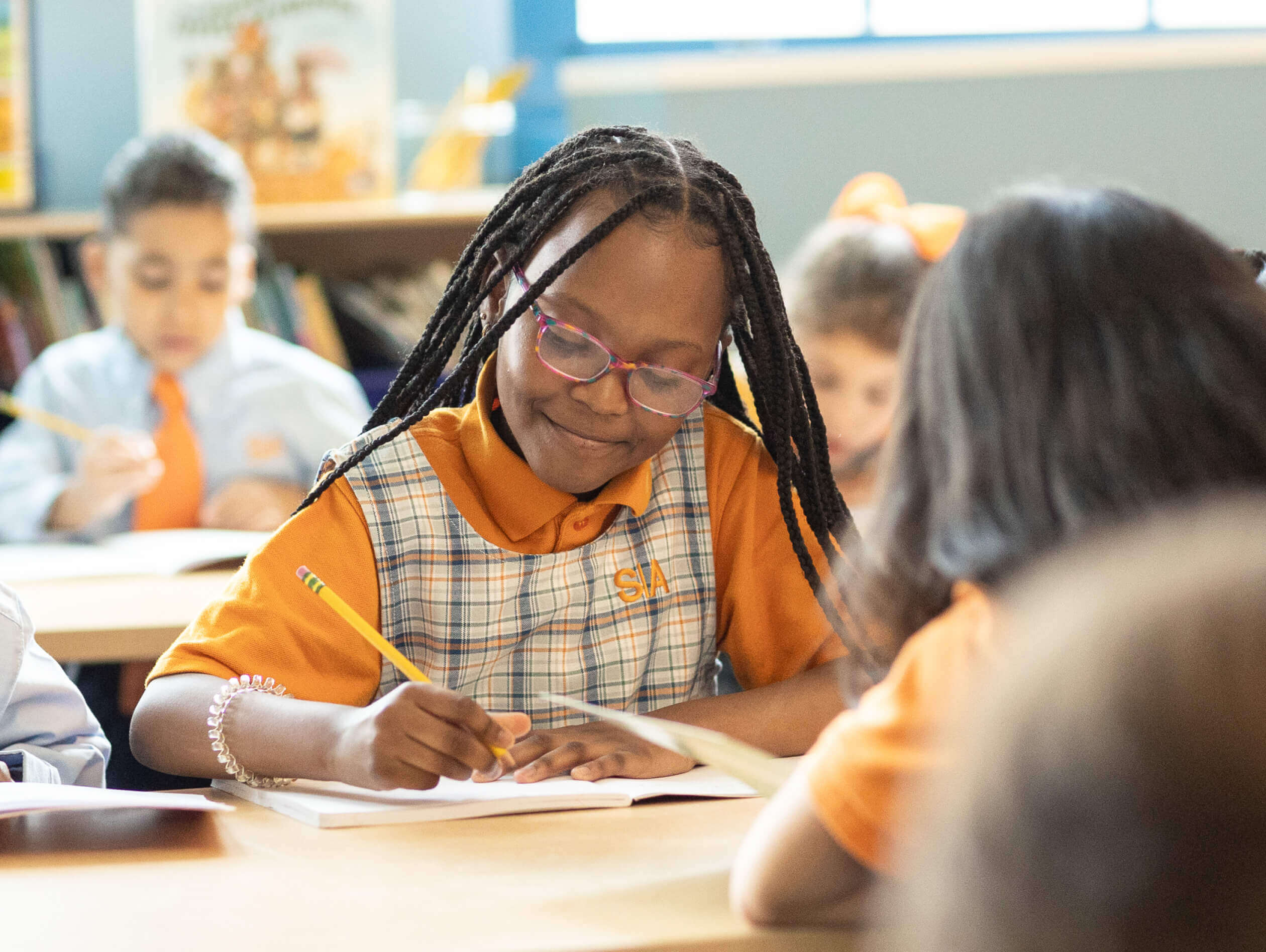A young girl writing in a notebook at a desk in a classroom.