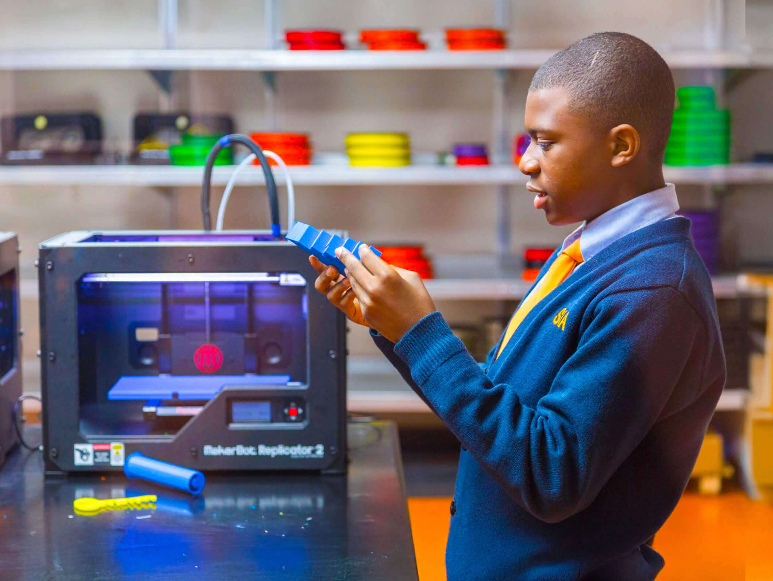 A student inspects a 3D printed blue object next to a 3D ﻿printer.